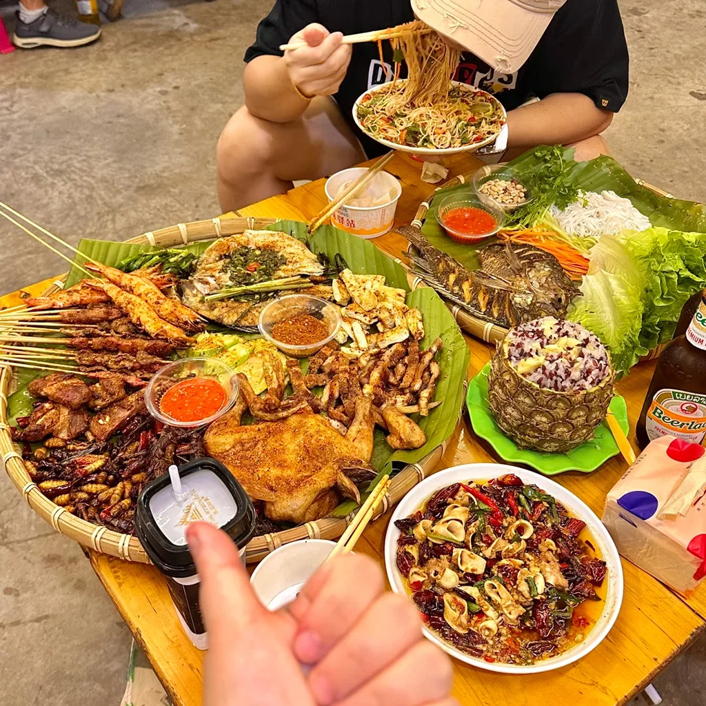 地道西雙版納傣味燒烤盛宴。烤魚、串燒、烤雞、菠蘿飯與香辣蘸料鋪在芭蕉葉上，是繽紛的雲南街頭美食。