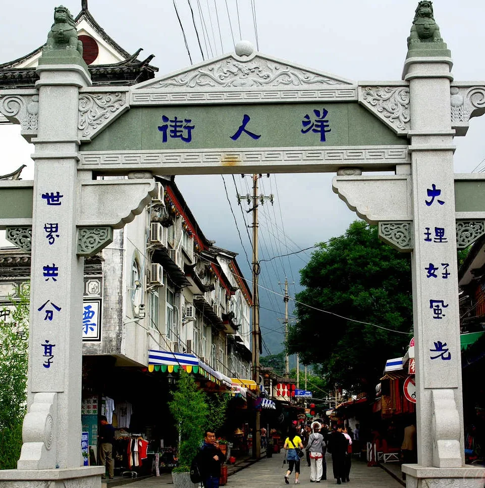 大理洋人街牌坊，傳統石雕門樓與街道景象，展現古城熱鬧氛圍。