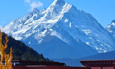 在 飛來寺 遠眺，雪山在陽光照耀下潔白耀眼，山峰巍峨聳立，前景建築與遠山形成層次分明的壯麗景觀。