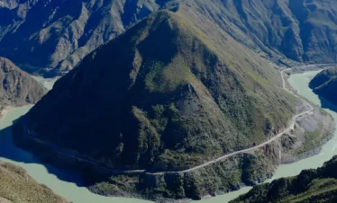 在 金沙江月亮湾 俯瞰，江水呈巨大弯曲环绕山体，宛如一轮弯月，公路沿山而行，景观壮丽震撼。