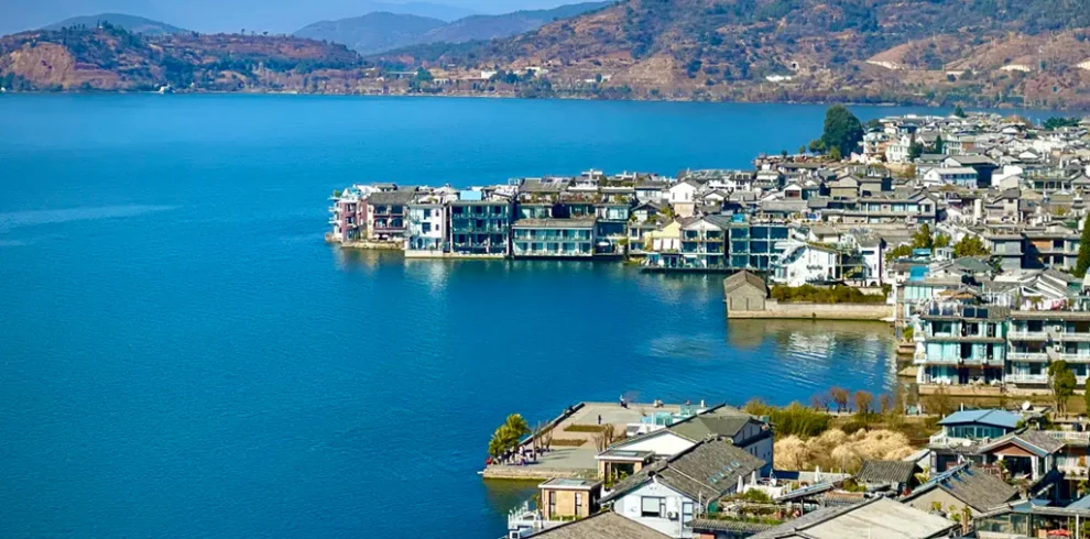 藍天碧水映襯下的 雙廊古鎮，湖岸建築錯落有致，展現靜謐悠閒風光。