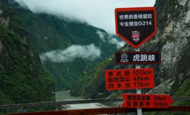 壯麗的 香格里拉虎跳峽 景色，翠綠峽谷被雲霧環繞，下方金沙江奔流，前方設有觀景路牌。