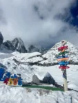 麗江玉龍雪山 4506 公尺高山觀景台，皚皚白雪覆蓋群山，木棧道蜿蜒山間，雲霧繚繞雪山峰巔，搭配城市距離指引牌。