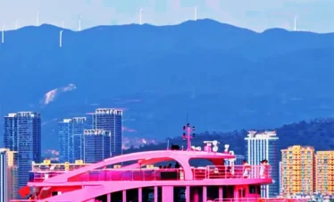 在 洱海 湖面上，一艘粉色遊艇緩緩航行，背景為大理城市建築與遠山景觀。