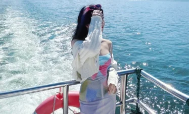 在 洱海 遊艇甲板上，一名女子迎著湖風站立，身後水花翻湧，遠方城市與群山相映。