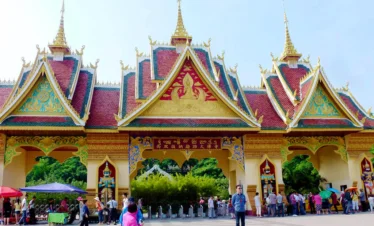 西雙版納勐泐大佛寺壯麗寺院入口景觀，金紅色屋頂與尖塔式建築展現濃厚南傳佛教與傣族建築風格，寺門雕刻精緻華麗，遊客在廣場前參觀拍照，呈現西雙版納著名佛教文化地標與宗教旅遊景點。