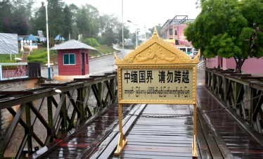 中緬邊境橋樑入口景象，橋面設有「中緬國界 請勿跨越」警示牌，周圍為邊境道路與哨所建築，展現中緬邊境地區的重要地理位置與跨國界線標誌