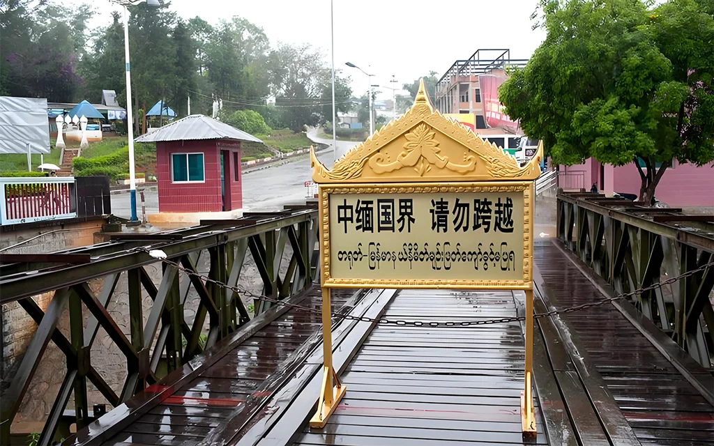 中緬邊境橋樑入口景象，橋面設有「中緬國界 請勿跨越」警示牌，周圍為邊境道路與哨所建築，展現中緬邊境地區的重要地理位置與跨國界線標誌