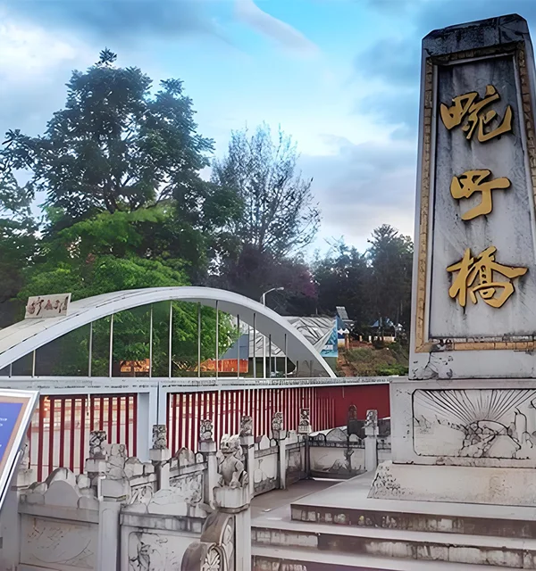 萬慶橋入口景觀，橋前立有刻著「萬慶橋」的石碑，旁邊是白色拱形橋體與紅色欄杆設計，周圍綠樹環繞與步道景觀，呈現邊境小鎮寧靜氛圍。此橋為當地具有歷史意義的地標之一，也是遊客參觀與拍照的熱門景點。
