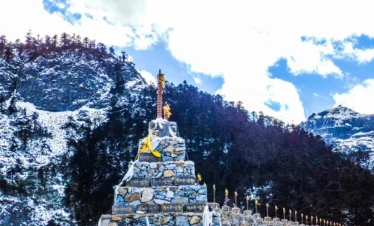 在 巴拉格宗大峡谷 雪山脚下，石堆经幡沿路排列，周围群山环绕，展现神圣而壮丽的高原峡谷景观。