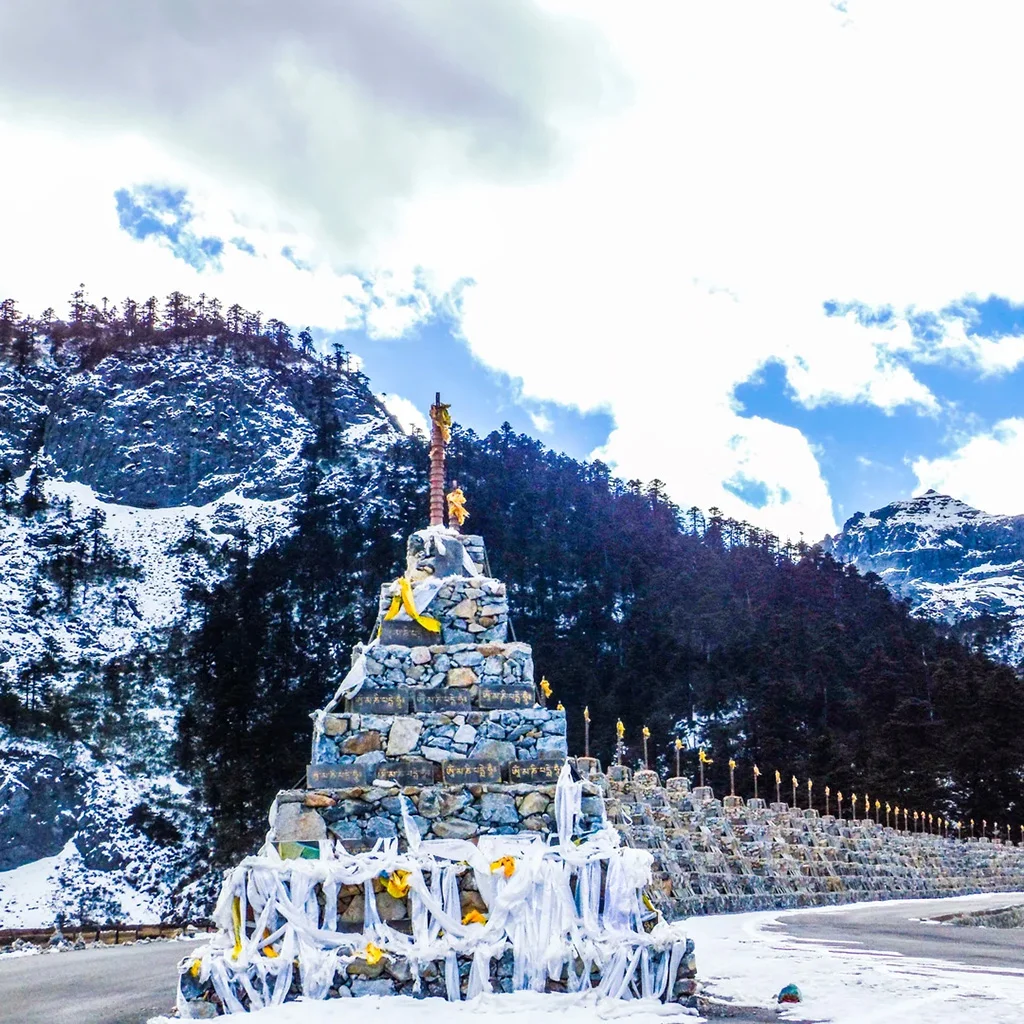 在 巴拉格宗大峡谷 雪山脚下，石堆经幡沿路排列，周围群山环绕，展现神圣而壮丽的高原峡谷景观。