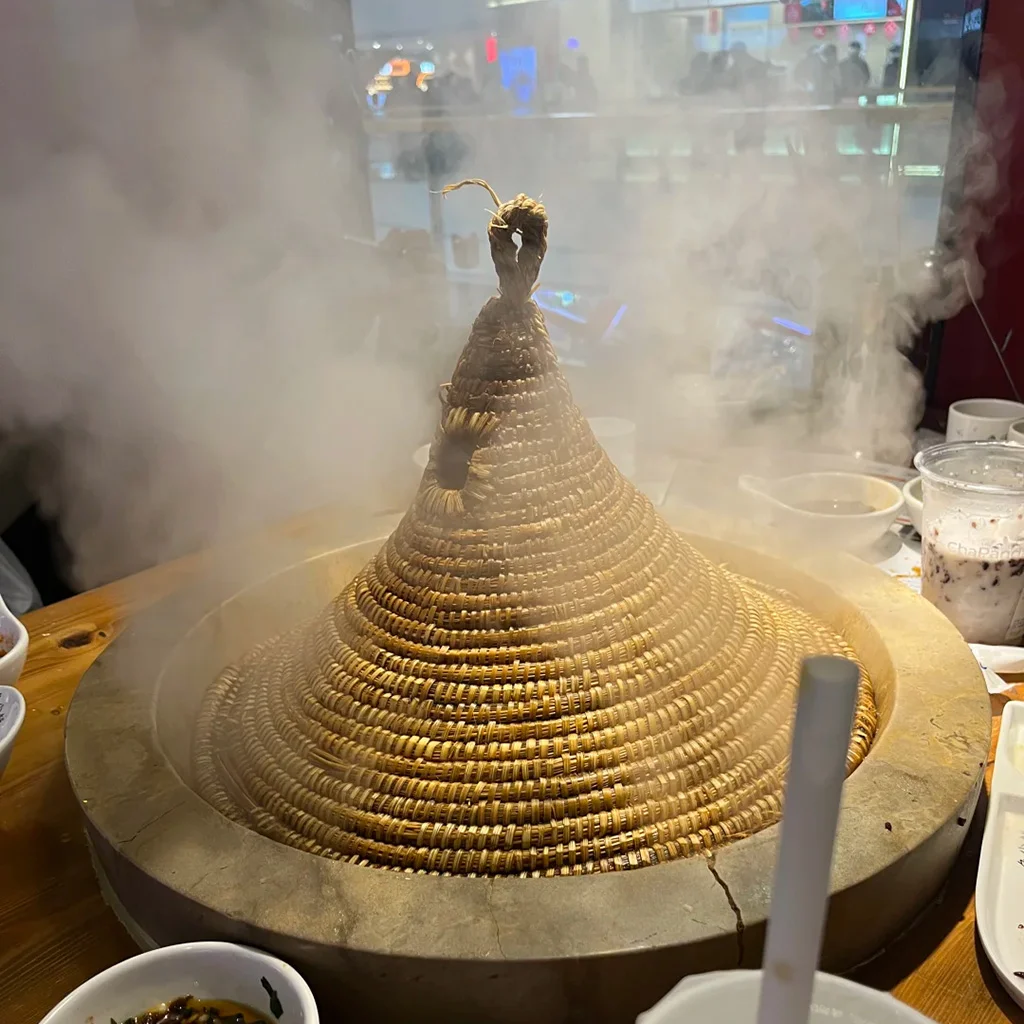 地道建水石鍋魚，雲南特色料理。新鮮魚類以手工雕刻石鍋蒸製，覆蓋編織圓錐草蓋，熱氣騰騰。