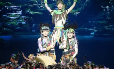 舞台表演《麗江千古情》中，演員身著民族服飾進行高難度疊人舞蹈，背景呈現森林幻境，燈光絢麗，展現麗江民族文化與藝術魅力。
