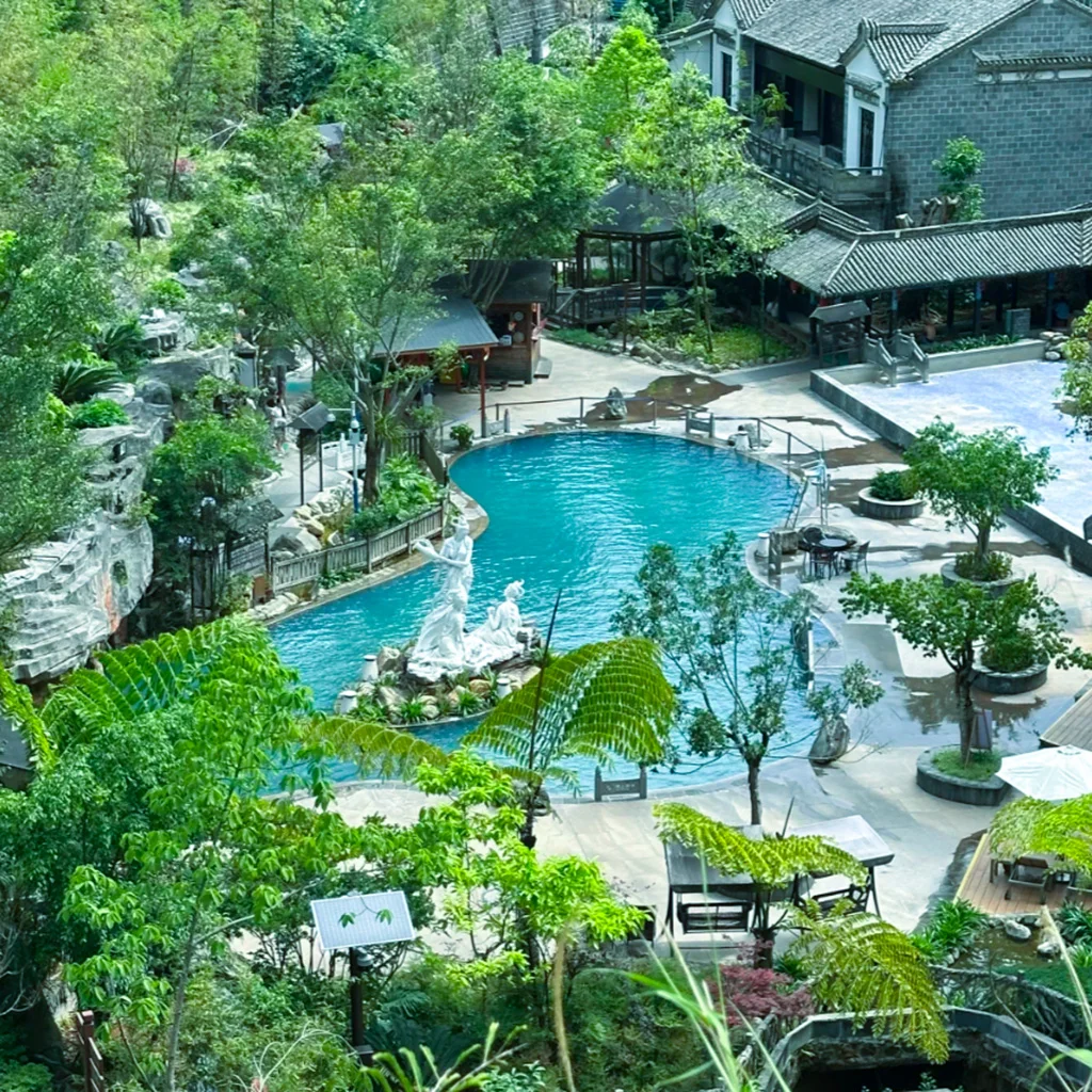 Rehai Scenic Area Tengchong City 騰沖市熱海風景區內的露天溫泉池景觀,藍色溫泉池中央設有雕像裝飾,周圍綠樹環繞並搭配中式建築與休憩步道,整體環境清幽雅致,展現騰沖熱海風景區結合自然景觀與溫泉文化的特色。