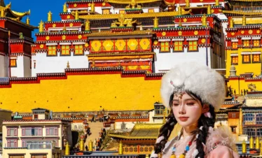 在 松贊林寺 前，遊客身著藏族傳統服飾拍照留念，金頂寺廟群莊嚴宏偉，色彩鮮豔，人物與藏式建築相互映襯，充滿民族風情。