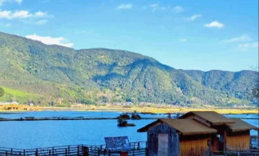 騰沖北海濕地自然景觀，湖面平靜映照藍天與群山，岸邊木屋與棧道延伸至水面，小船整齊停泊於碼頭旁。遠方青山環繞濕地湖泊，展現騰沖北海濕地獨特的高原湖泊生態與寧靜優美的自然風光