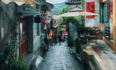 騰沖和順古鎮石板街巷景觀，兩側為傳統中式建築與特色店鋪，紅燈籠與庭院綠植點綴其間，遠處可見山景與遊客漫步其間，展現古鎮悠閒氛圍與濃厚歷史文化氣息。