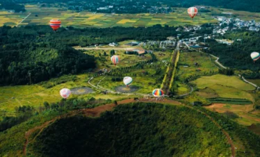 騰沖火山地熱國家地質公園壯觀火山口地形與熱氣球景觀，從高空俯瞰完整火山錐與綠色森林環繞，多彩熱氣球緩緩升空，遠處田園與山巒相連，展現騰沖火山地熱國家地質公園獨特火山地貌與自然生態景觀。