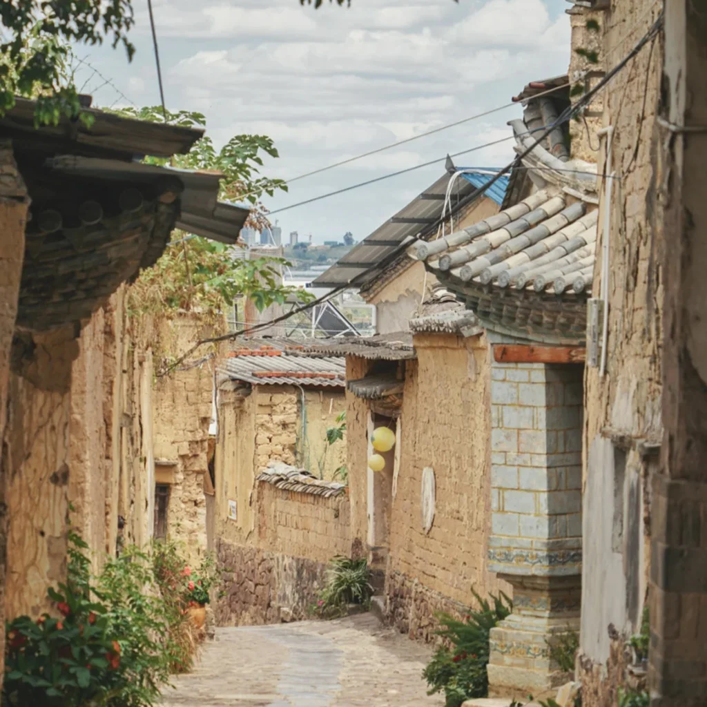 雲南團山民宅古村巷道景觀，狹窄石板路兩側是傳統土牆與瓦頂民居，老屋牆面帶有歲月痕跡，屋簷與綠植相互點綴，展現團山民宅保存完整的歷史建築與寧靜古村生活氛圍
