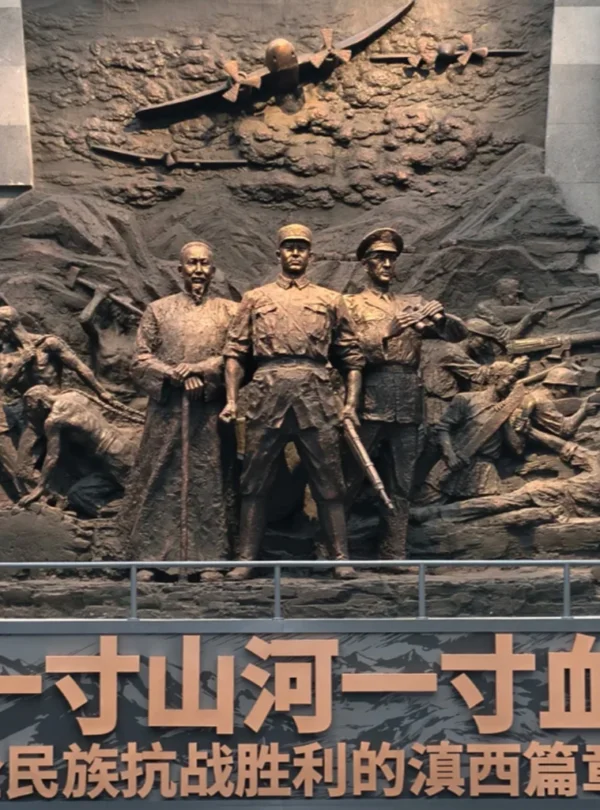 滇西抗戰紀念館大型歷史浮雕雕塑，呈現抗日戰爭時期軍民並肩作戰的場景，中央人物象徵指揮與守護家園的決心，上方飛機與戰士形象重現滇西戰場的激烈戰鬥與歷史記憶。