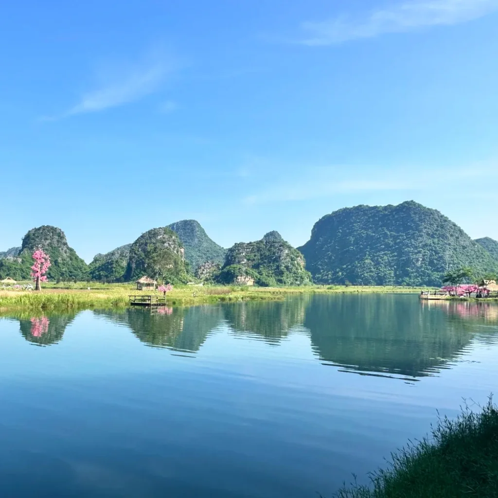 普者黑拍攝地壯麗的綠色喀斯特山丘倒映在平靜的藍色湖泊中，岸邊點綴著粉紅色的桃花樹。