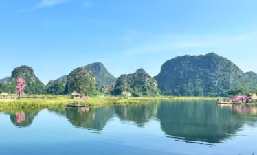 普者黑拍攝地壯麗的綠色喀斯特山丘倒映在平靜的藍色湖泊中，岸邊點綴著粉紅色的桃花樹。