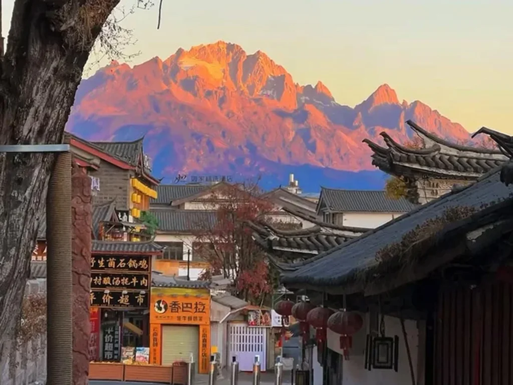 Shuhe Ancient Town 1 麗江古城眺望玉龍雪山的絕美「機位」,清晨日出時刻,雪山被金紅霞光染成「日照金山」奇景,前景是古色古香的納西建築。
