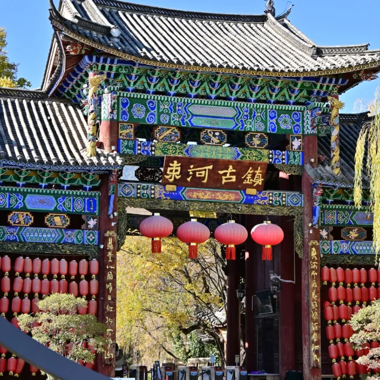 麗江束河古鎮大門牌樓，彩繪雕花古建飛檐，滿掛喜慶紅燈籠，在湛藍晴空下盡顯千年納西古韻。