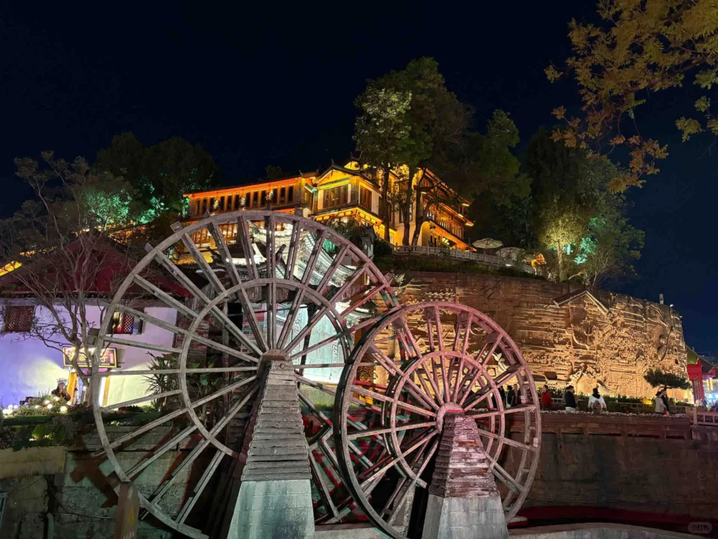 The Giant Water Wheel of Lijiang Ancient Town 麗江古城大水車夜景,巨型木製水車佇立於夜空中,背景是點燈的傳統納西建築與石雕牆。
