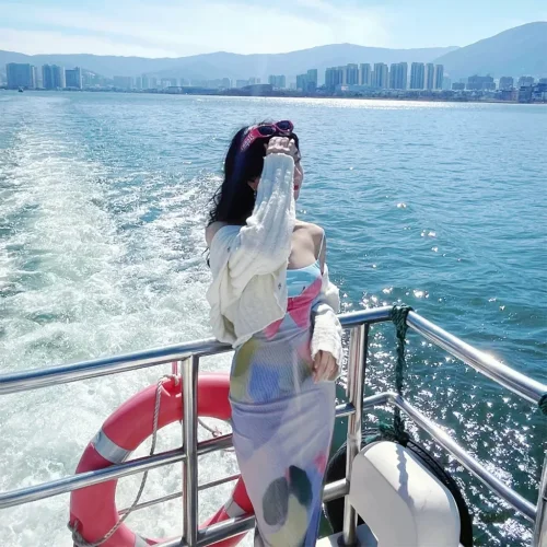 Erhai Yacht2 在 洱海 遊艇甲板上,一名女子迎著湖風站立,身後水花翻湧,遠方城市與群山相映。