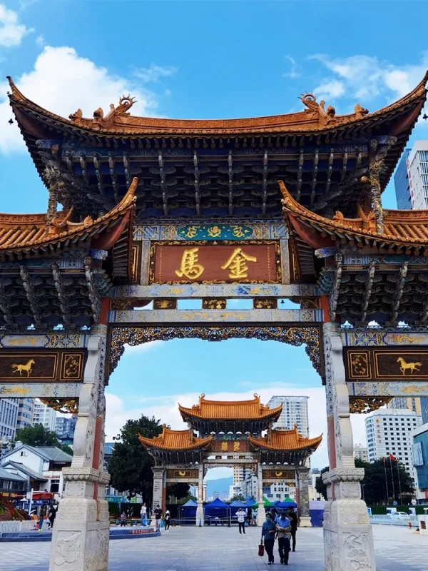 Kunming Jinma Biji Archway 昆明金馬碧雞坊矗立於廣場,藍天下的傳統建築展現飛簷翹角與精美彩繪。牌坊刻有「金馬」字樣,與後方現代城市建築交織。