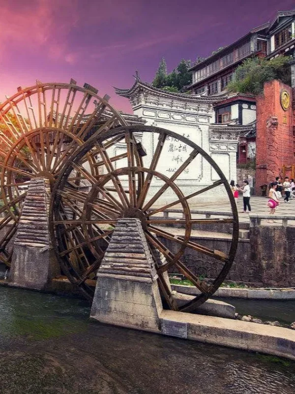 麗江古城著名的大水車景觀，巨大的木製水車在清澈河道旁緩緩轉動，周圍是傳統納西族建築與古城街景。