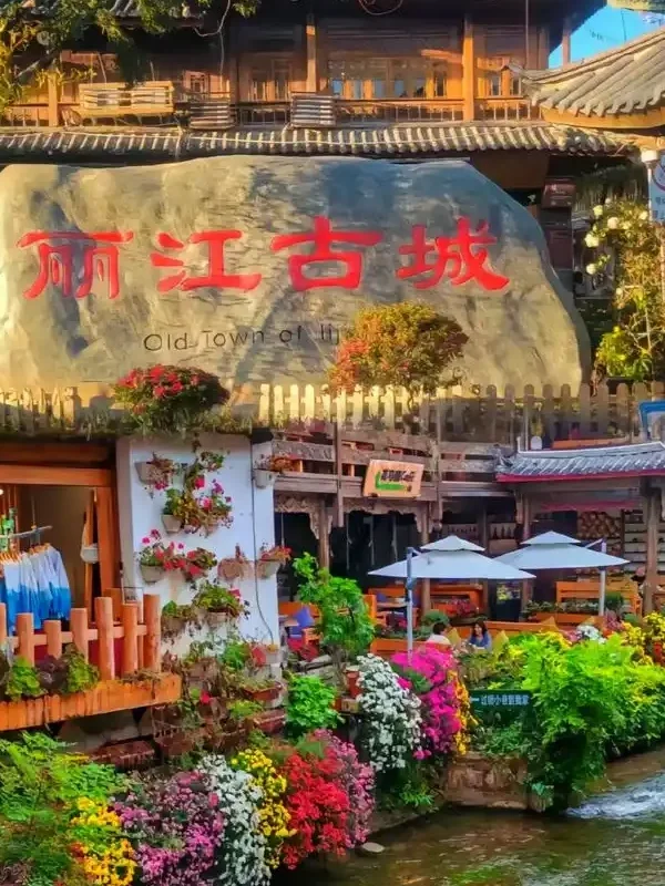 麗江古城著名的大水車景觀，巨大的木製水車在清澈河道旁緩緩轉動，周圍是傳統納西族建築與古城街景，遊客漫步其間，展現麗江古城融合歷史文化與自然水景的特色風光。